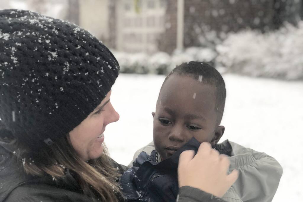 Christy Lillie holding a young child in her arms and zipping up his winter coat as snow falls around them.